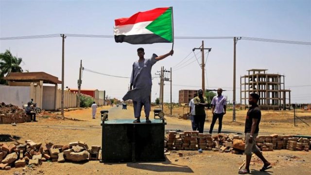 A Sudanese protester holds a national flag as he stands on a street barricade, demanding that the country's Transitional Military Council hand over power to civilians, in Khartoum on June 5 [Reuters]