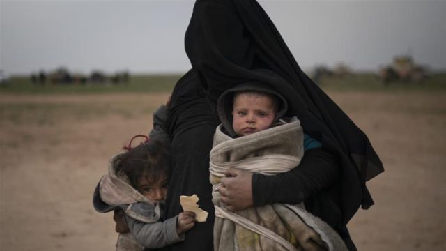 A woman evacuated from the last territory held by ISIL militants carries two children after being screened by the SDF outside Baghouz, Syria on February 26, 2019 [File: AP/Felipe Dana] [Daylife]