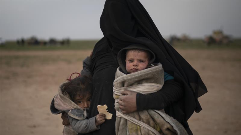 A woman evacuated from the last territory held by ISIL militants carries two children after being screened by the SDF outside Baghouz Syria