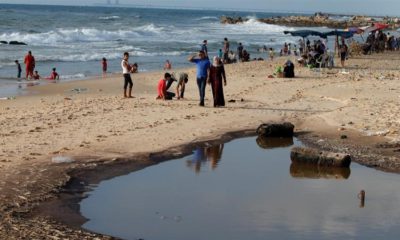 Palestinians walk past a pool of sewage on a beach in the northern Gaza Strip