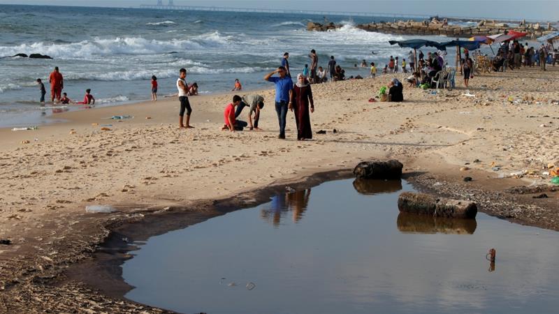 Palestinians walk past a pool of sewage on a beach in the northern Gaza Strip