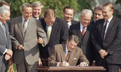 Congresspeople watch closely as President Ronald Reagan signs into law a landmark tax overhaul on the South Lawn of the White House in Washington