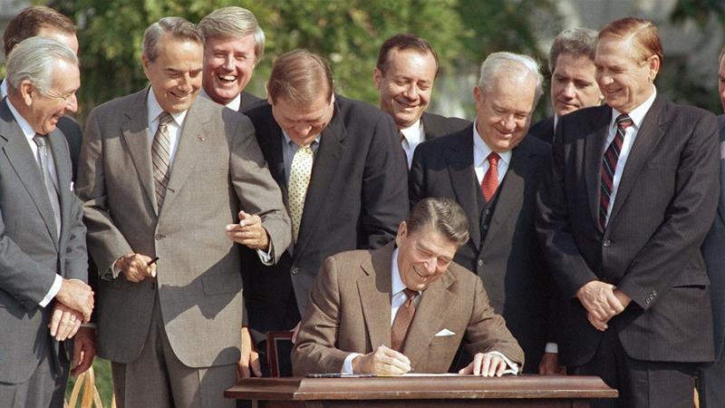 Congresspeople watch closely as President Ronald Reagan signs into law a landmark tax overhaul on the South Lawn of the White House in Washington