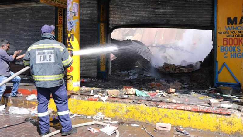 A shopkeeper watches as a fireman douses a burned and damaged property after overnight unrest and looting in Johannesburg