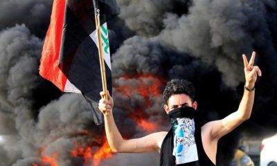 A demonstrator gestures as he stands close to burning tyres blocking a road during a protest in Baghdad, Iraq, October 2, 2019 [File: Thaier al-Sudani/Reuters]