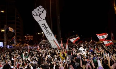 Protesters use their mobile phones as a structure representing a fist is erected to replace a previous one that was burnt at Martyrs Square in Beirut