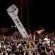 Protesters use their mobile phones as a structure representing a fist is erected to replace a previous one that was burnt at Martyrs Square in Beirut