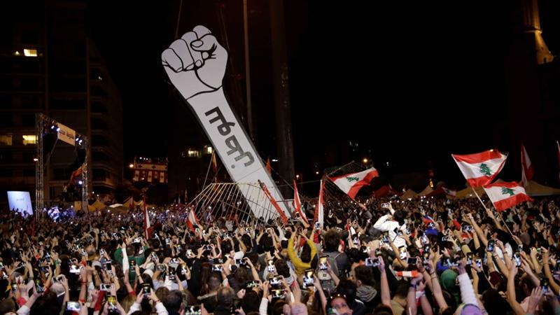 Protesters use their mobile phones as a structure representing a fist is erected to replace a previous one that was burnt at Martyrs Square in Beirut