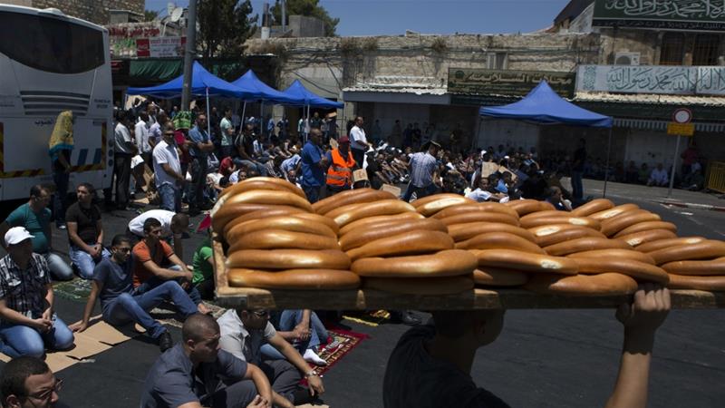A youth walks by carrying loaves of bread as worshippers prepare to pray close to the Damascus Gate of the Old City in Jerusalem on July 25 2014
