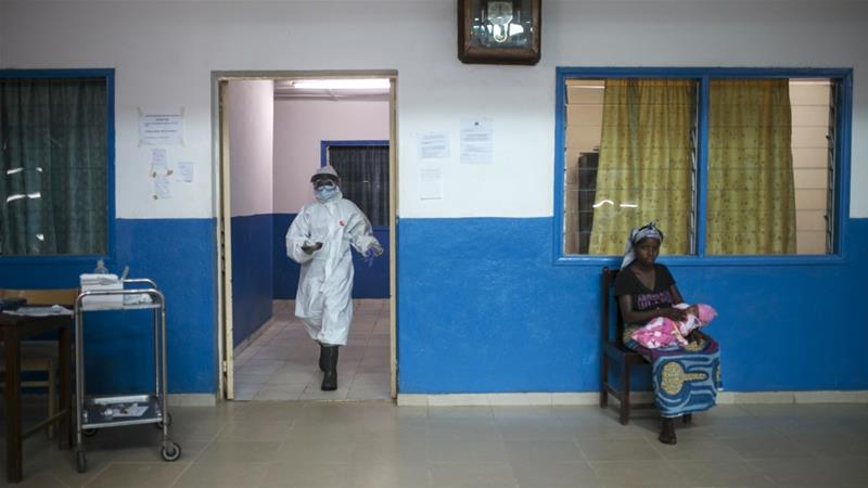 A health worker walks past a woman holding a baby at the maternity ward in the government hospital in Koidu Kono district in eastern Sierra Leone on December 20 2014