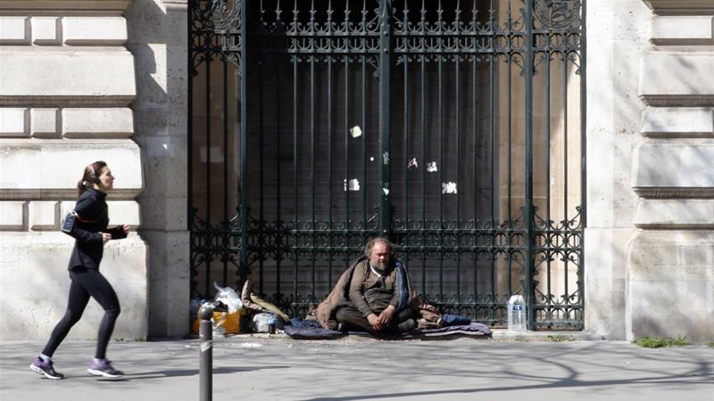 A woman runs as a homeless man looks on during the lockdown of coronavirus in Paris on March 27 2020