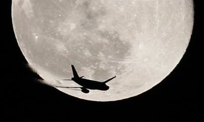 An airplane is silhouetted against the full Moon