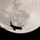 An airplane is silhouetted against the full Moon