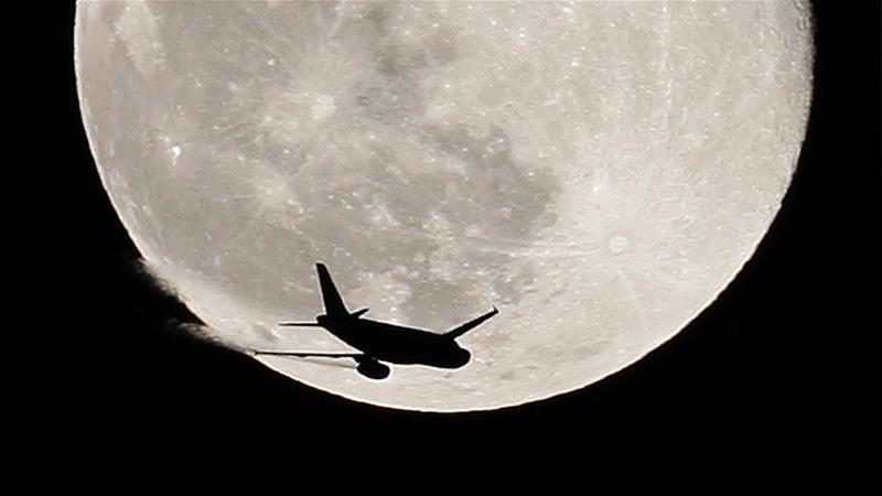 An airplane is silhouetted against the full Moon