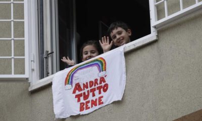 Children wave after placing a banner reading Everything will be all right out of the window of their apartment in Rome Italy on March 13 2020