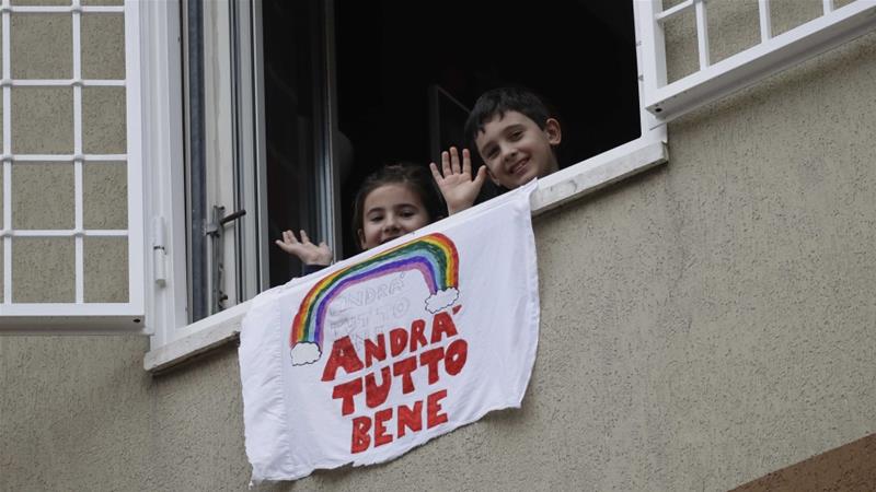 Children wave after placing a banner reading Everything will be all right out of the window of their apartment in Rome Italy on March 13 2020