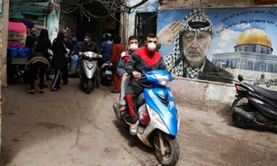 People wear face masks as they drive past a poster depicting late Palestinian leader Yasser Arafat in Shatila refugee camp in Beiruts suburbs Lebanon on March 30 2020