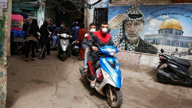 People wear face masks as they drive past a poster depicting late Palestinian leader Yasser Arafat in Shatila refugee camp in Beiruts suburbs Lebanon on March 30 2020