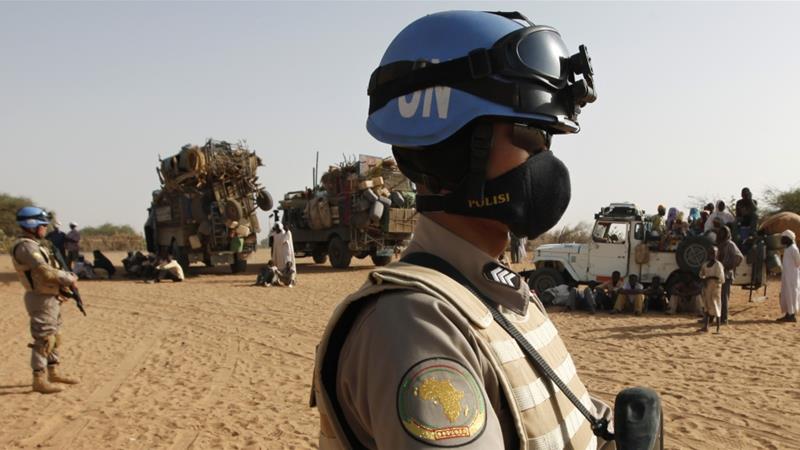 Two UNAMID peacekeepers patrol by trucks loaded with new arrivals of displaced Sudanese at Zamzam refugee camp outside the Darfur town of al Fasher Sudan on March 23 2009