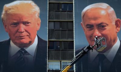 A labourer stands on a crane as he puts up banners depicting US President Donald Trump and Israeli Prime Minister Benjamin Netanyahu in Jerusalem on June 10 2020