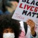 A woman wearing a protective face mask holds a banner as she attends a protest against police brutality at Place de la Republique in Lille France June 10 2020