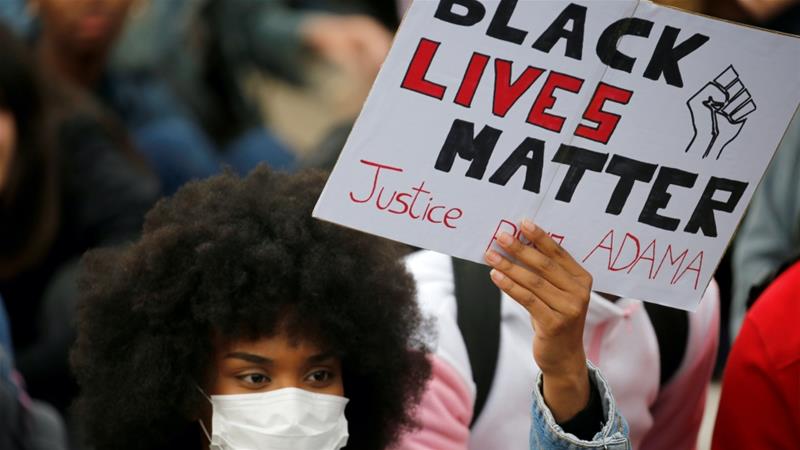 A woman wearing a protective face mask holds a banner as she attends a protest against police brutality at Place de la Republique in Lille France June 10 2020