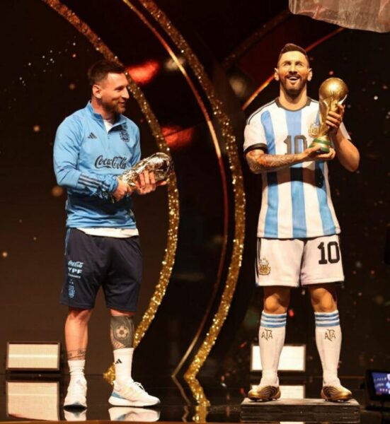 Lionel Messi with a statue of himself holding the World Cup